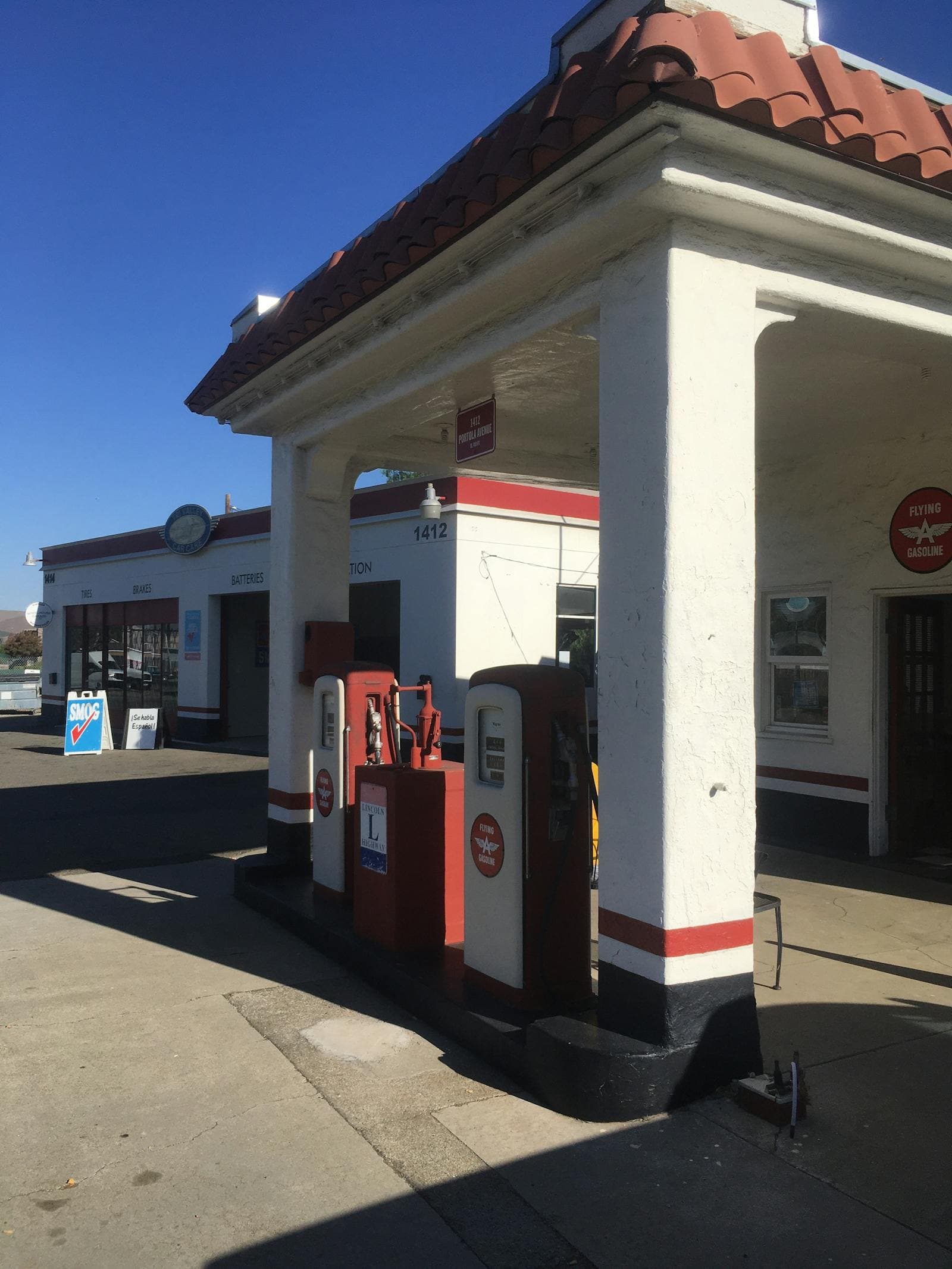 A vintage mid-century gas station with red-and-white painted pumps under a deep blue sky